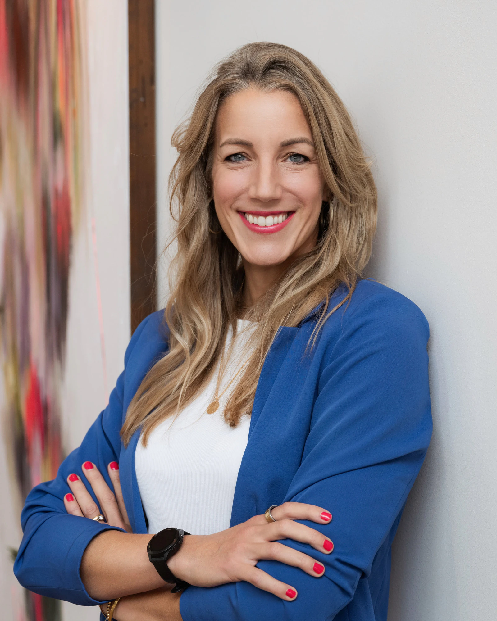 Porträt von Dr. Simone Kreyer: eine lächelnde Frau mit langen blonden Haaren, blauem Blazer und verschränkten Armen an einer hellen Wand.